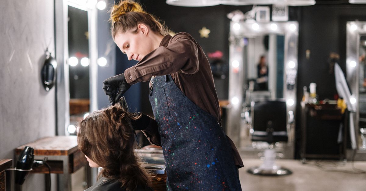 A female stylist expertly applying hair color to a client in a modern salon setting.
